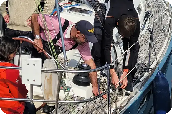 Alumnado trabajando con cabos y winches en cubierta durante las prácticas oficiales de navegación a vela