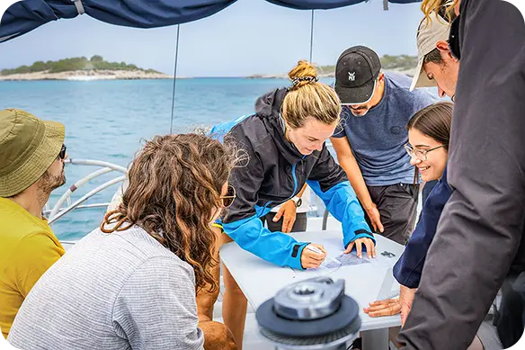 Estudiants d'Escola Port a bord d'un dels velers escola realitzant exercicis de carta de navegació durant les pràctiques de navegació.