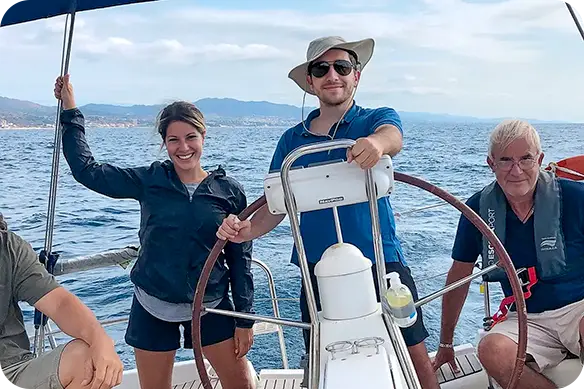Alumnos a bordo de un velero, al timón, durante una salida de navegación al Mediterráneo, realizando el curso para bordo